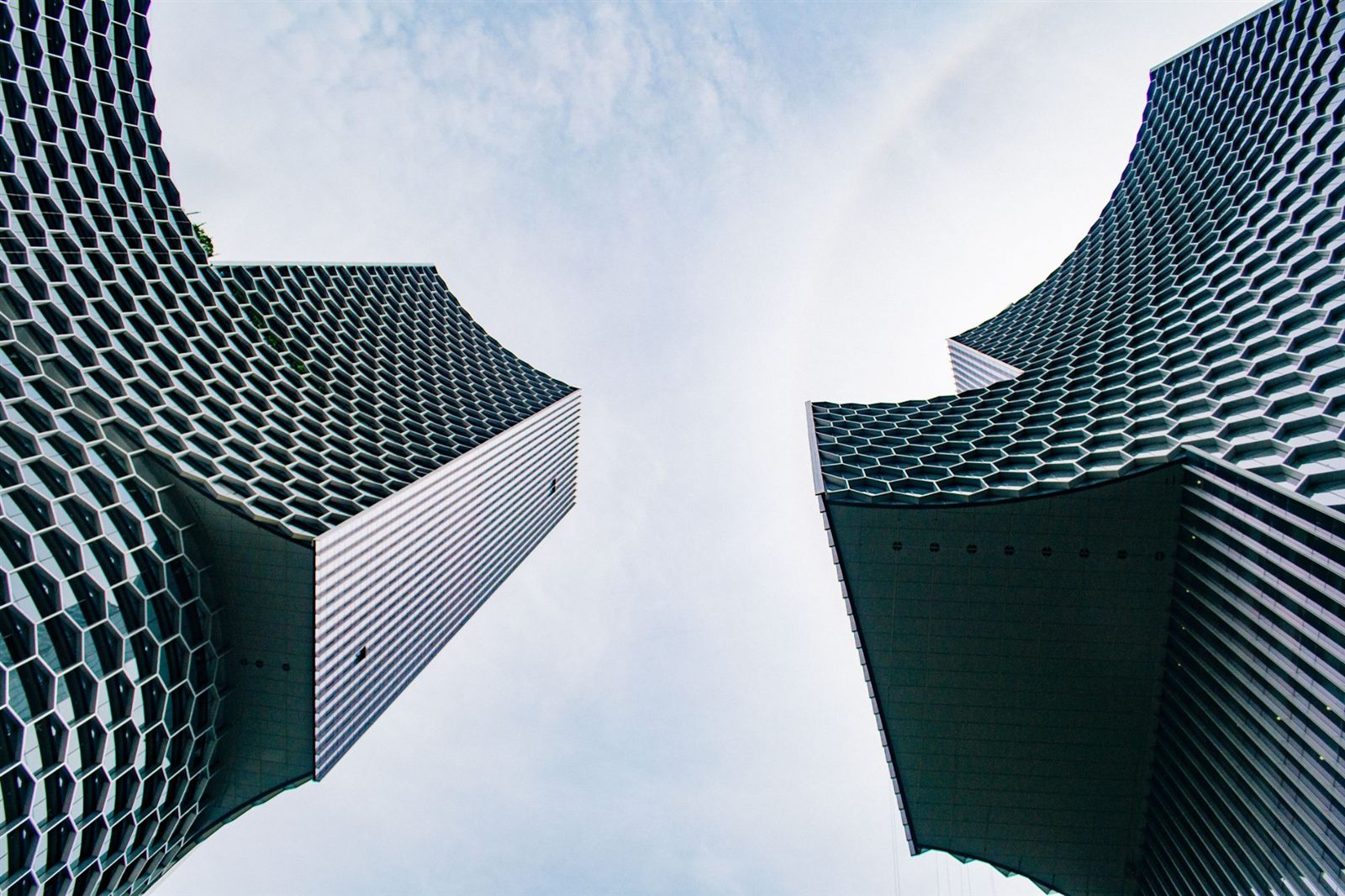 Two towers with honeycomb facades seen from below against a cloudy sky