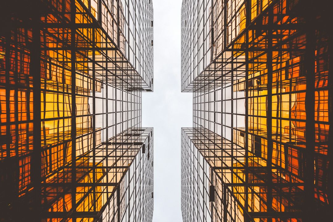 Two glass office towers seen from below, their windows reflecting an orange sunset